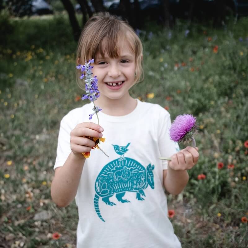 A young girl holding flowers wearing an armadillo shirt.