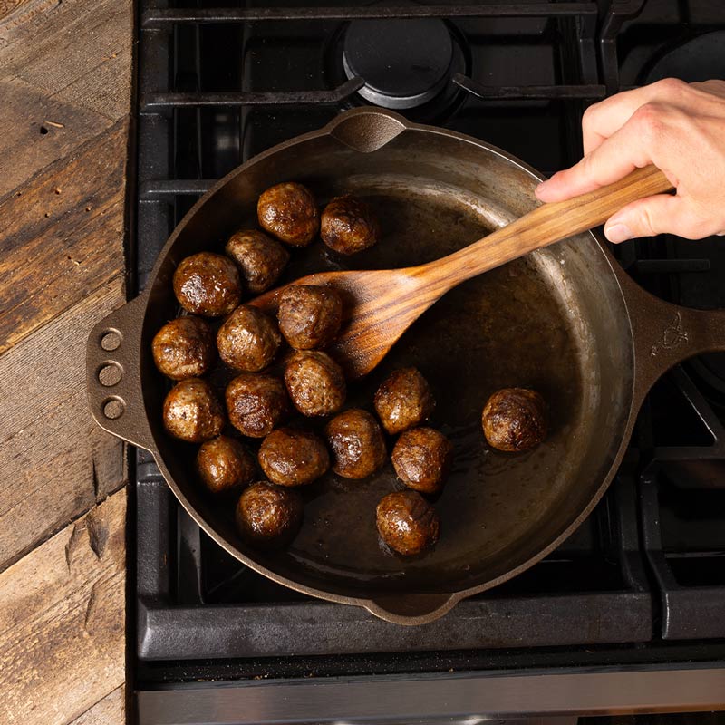 Meatballs cooking in a cast iron pan.