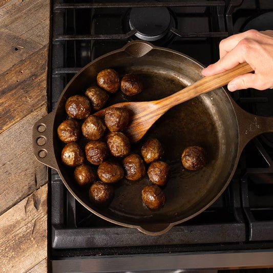Meatballs cooking in a cast iron pan.