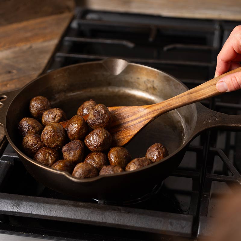 Meatballs cooking in a cast iron pan.