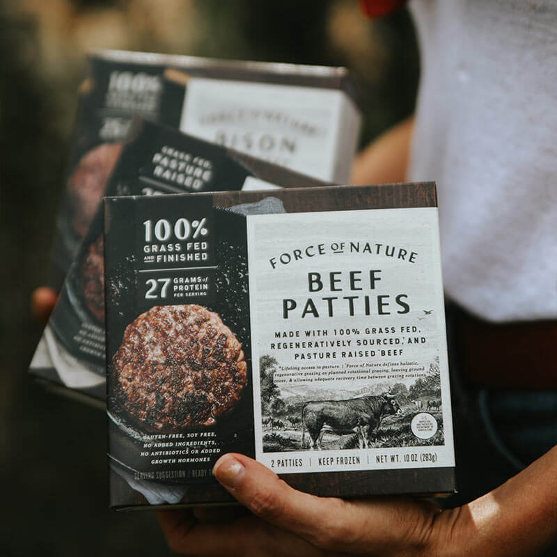 A person holding boxes of Force of Nature beef patties.