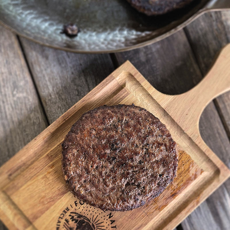 Burger patty on a wooden cutting board.