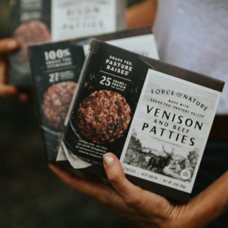 A person holding boxes of Venison patties.