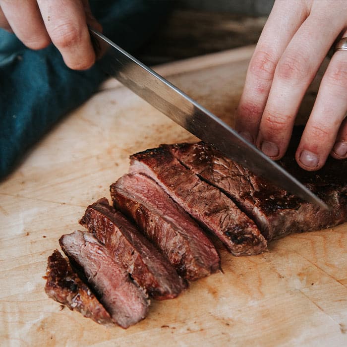 Cooked NY Strip Steak being sliced on a wooden cutting board.