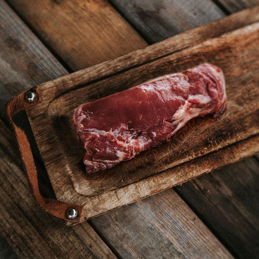 Raw NY Strip Steak on a wooden cutting board.