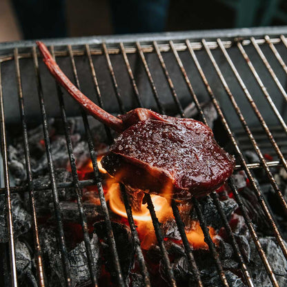 Tomahawk steak cooking on a grill.