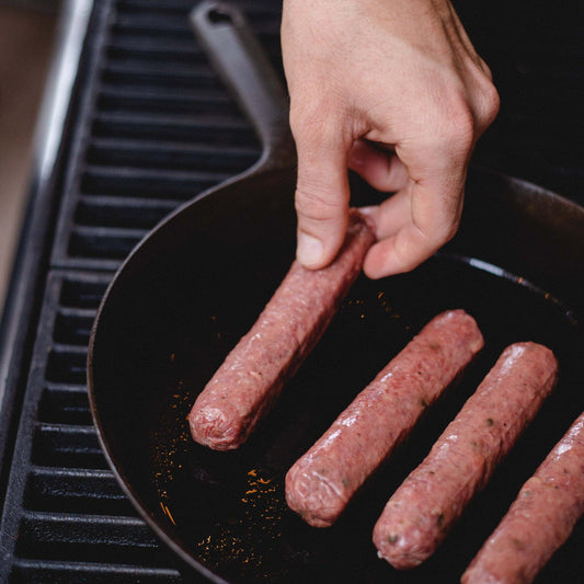 Sausages being placed in a cast iron pan.